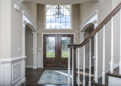 An open foyer with cream white walls, dark brown hardwood floors and door.