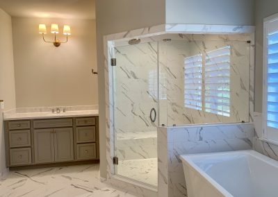 A large walk-in shower with a glass door and matching tile with the floor. A large bathtub is next to it.